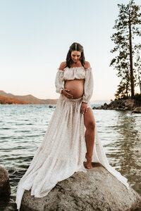 A pregnant woman in a beautiful two piece gown standing on a boulder at Lake Tahoe.