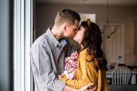 Luxury Maternity and Newborn Portraits by Moving Mountains Photography in NC -Photo of a couple kissing while holding their newborn baby.