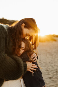 A mother and her daughter hugging at sunset wearing their favourite winter knitwear, they have their eyes closed and they look extremely relaxed and happy while christchurch photography lucy jane captures them in her camera