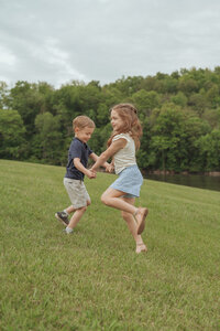 A brother and sister play together in a field of grass next to water and trees at Winged Deer Park in Johnson City TN. Taken by a Northeast TN photographer. 