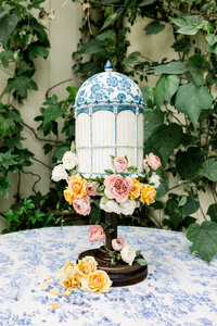 bird cage wedding cake with sugar wafer flowers on cake stand on blue vintage tablecloth, photo by Anastasiya Photography - London Wedding Photographer