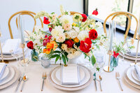 Bright and colorful wedding table setting with red, orange, and cream florals styled by an Austin wedding planner for a vibrant Hill Country celebration.