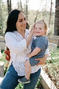 woman caressing the face of her toddler while standing in her garden