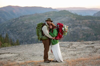 Newlyweds hug with backpacking packs on while on top of a granite dome in Yosemite.