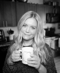 A nutritionist woman holding a white coffee mug and softly smiling at the camera.