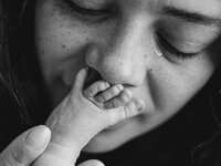 black and white image of woman kissing newborn infant foot up to her mouth while tear falls from her eye by Portland Family Photographer Emilie Phillipson Photography