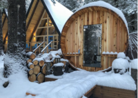 An A-frame cabin sits next to a round wooded sauna in the forest in Seward, AK.