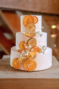 Three-tier wedding cake decorated with dried orange slices.