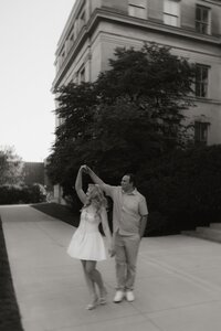 A man twirls his fiancé in her short white dress during their engagement session.