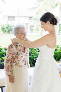 A newlywed in a wedding dress playing a lei over their grandparent 