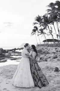 A newlywed couple in wedding dresses kissing on a beach 
