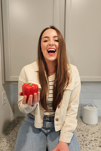 Lauren Mashall of Bodyfit Nutrition sits on a kitchen counter smiling at the camera with a red pepper in her hand.