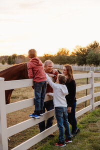 A family standing next to a fence as they pet a horse