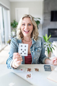 Entrepreneur wearing jean jacket in bright modern kitchen holding playing card to camera.