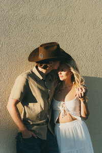 Western couple embracing in soft window light wearing cowboy hats during their intimate session