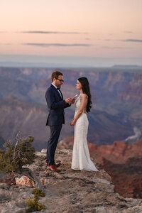 Bride and groom celebrating their Grand Canyon elopement on a cliff edge, with hands raised in joy and the canyon stretching out below them