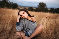 Senior Photography, girl sitting in field with her head tilted to the side