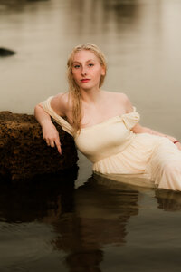 Senior girl in an off-shoulder dress posing in a calm lake during a natural light portrait session in Minneapolis