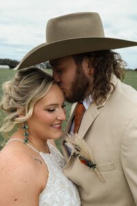 Wedding shoot with groom kissing bride on the forehead in a field of grass