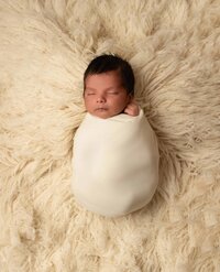 Baby wrapped on table with beautiful lighting in Hello Little Prop's Olive Green Backdrop and Wrap set.