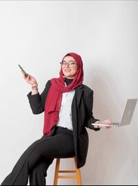 Ayah Official smiling while holding a laptop and phone, representing her role as a business mentor helping women entrepreneurs build authority and sustainable online growth.