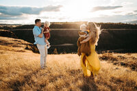 Parents standing and holding  their kids in each arm at field during golden hour