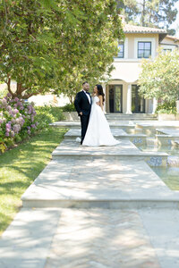 A photo of the bride and groom posing in front of a Mediterranean home. 