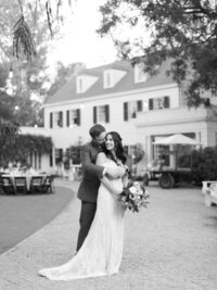 black and white photo of bride and groom in front of manor