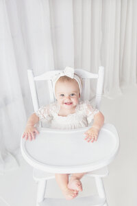 Baby girl sitting on wood high chair during cake smash photoshoot in Mount Juliet tennesse photography studio