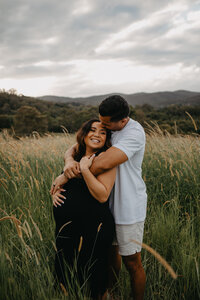 husband hugs pregnant wife in a field on the gold coast