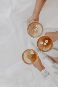 white sheet background with hands of three girls holding cocktails with small daisy flowers in the drinks