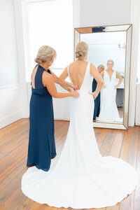 Mother of the bride buttoning the bride's wedding gown as she prepares for her wedding day