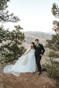 Bride and groom standing on the edge of a mountian looking off into the distance