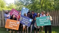 Boss & Buddha Founder standing with large group of people celebrating as coworkers holding Certified B Corporation company signs