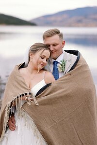Wedding and Elopement Photography,  bride and groom embrace in front of alpine lake during Rocky Mountain elopement.