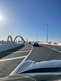 View from inside a luxury sports car driving across Tokyo’s Rainbow Bridge under clear blue skies, heading toward the city skyline.