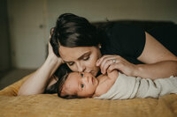 Mom kissing her newborn son while lay down on a bed in their house in Vancouver, WA