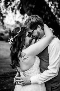 Black and white photo of a bride and groom embracing closely, smiling with their foreheads touching during a quiet moment outdoors