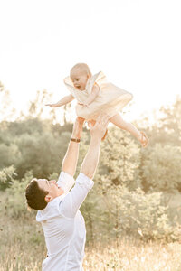 Dad throwing baby girl up in the air. Both are wearing light neutral tones and colors. Portland Family Photography session.