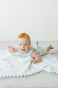 Baby lying on stomach on a white blanket, smiling at the camera