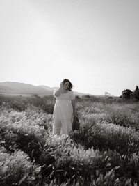 Silhouette of an expectant mother standing in tall grass with mountains behind her, in black and white.