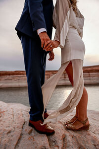 A romantic engagement proposal amidst the soft golden sand dunes near Lake Powell, with the clear lake and towering cliffs in the background.