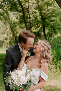 Newlyweds standing behind each other leaning in for a kiss