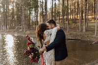 bride and groom kissing in a forest in front of a lake