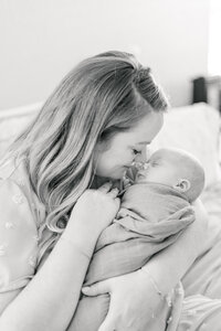 a mother goes nose to nose with her newborn baby in this black and white photograph.