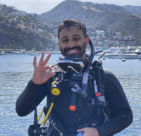 Smiling scuba diver on the surface gives the underwater ok symbol while in his full wet suit