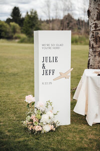 Custom calligraphy wedding welcome sign featuring florals, column and airplane details representing full service design and calligraphy by Life in Letters.