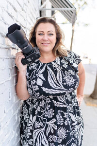 Renee Warren wearing black top and pink skirt leaning on railing and smiling at camera