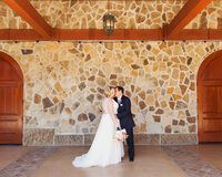 Full body portrait of Groom kissing Bride as she holds her bouquet