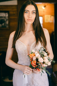 Woman with a wedding jumpsuit and a bouquet in her hands looking at the camera.